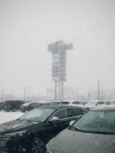 snowy parking lot with cars in the foreground and a business sign in the background