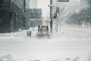 Snowy city street corner with small skid steer plowing snow on sidewalk